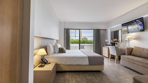 A hotel room with a bed, a desk, a sofa, a TV, and a balcony with a view. - Akti Palace Hotel - All inclusive (Kos)