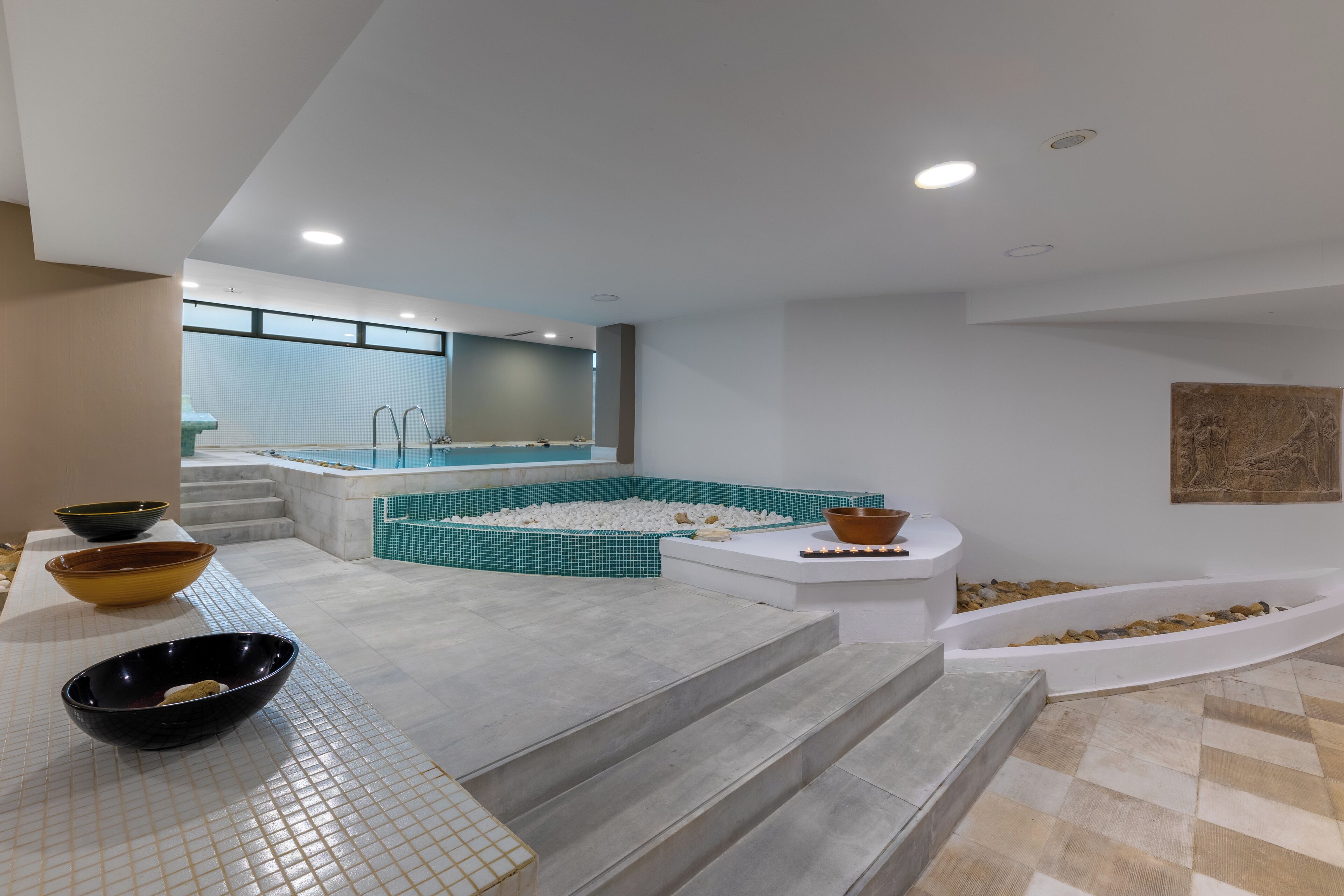 Un baño moderno con una bañera grande, una zona de estar con suelo de mosaico y un conjunto de escaleras que llevan a una zona de ducha.