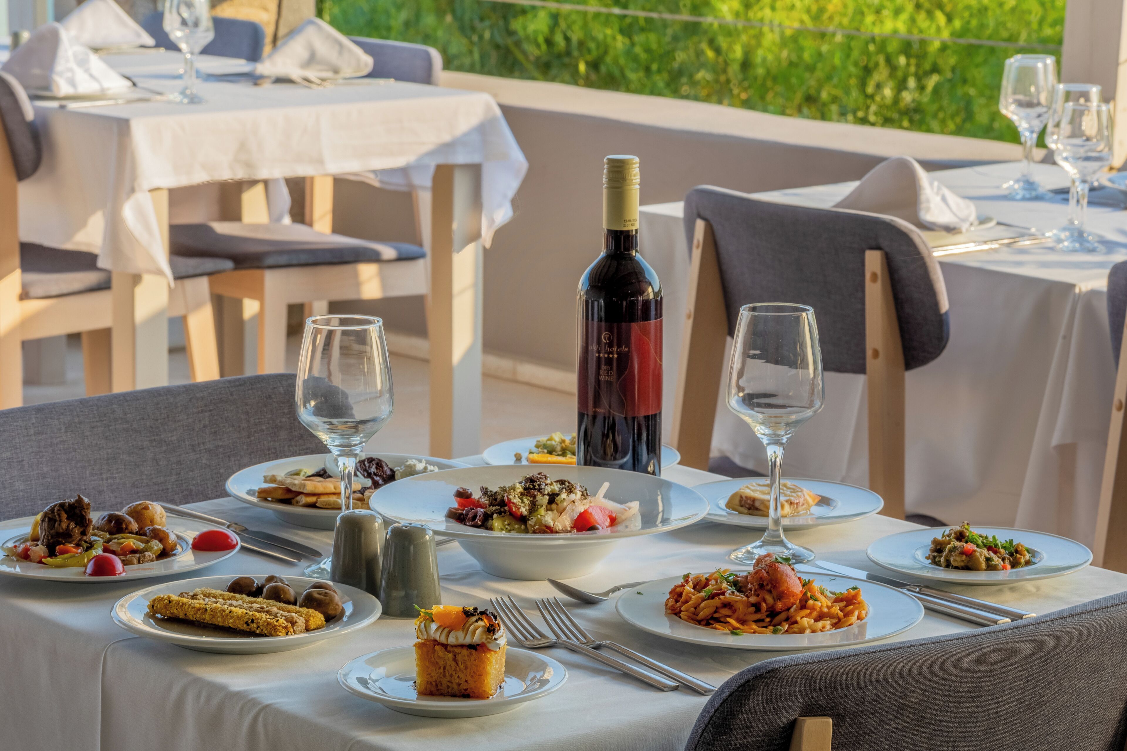 Un área de comedor al aire libre con varias mesas preparadas para comidas, cada una con platos de comida, copas de vino y cubiertos.