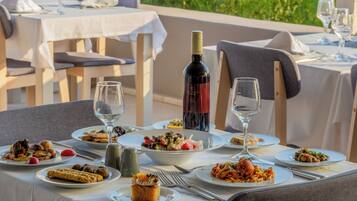 Un área de comedor al aire libre con varias mesas preparadas para comidas, cada una con platos de comida, copas de vino y cubiertos.
