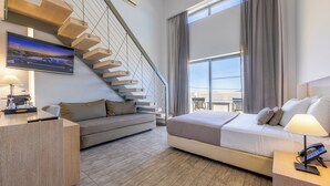 A modern hotel room with a built-in bed, a sofa, a desk, and a staircase with a TV screen. - Akti Palace Hotel - All inclusive (Kos)