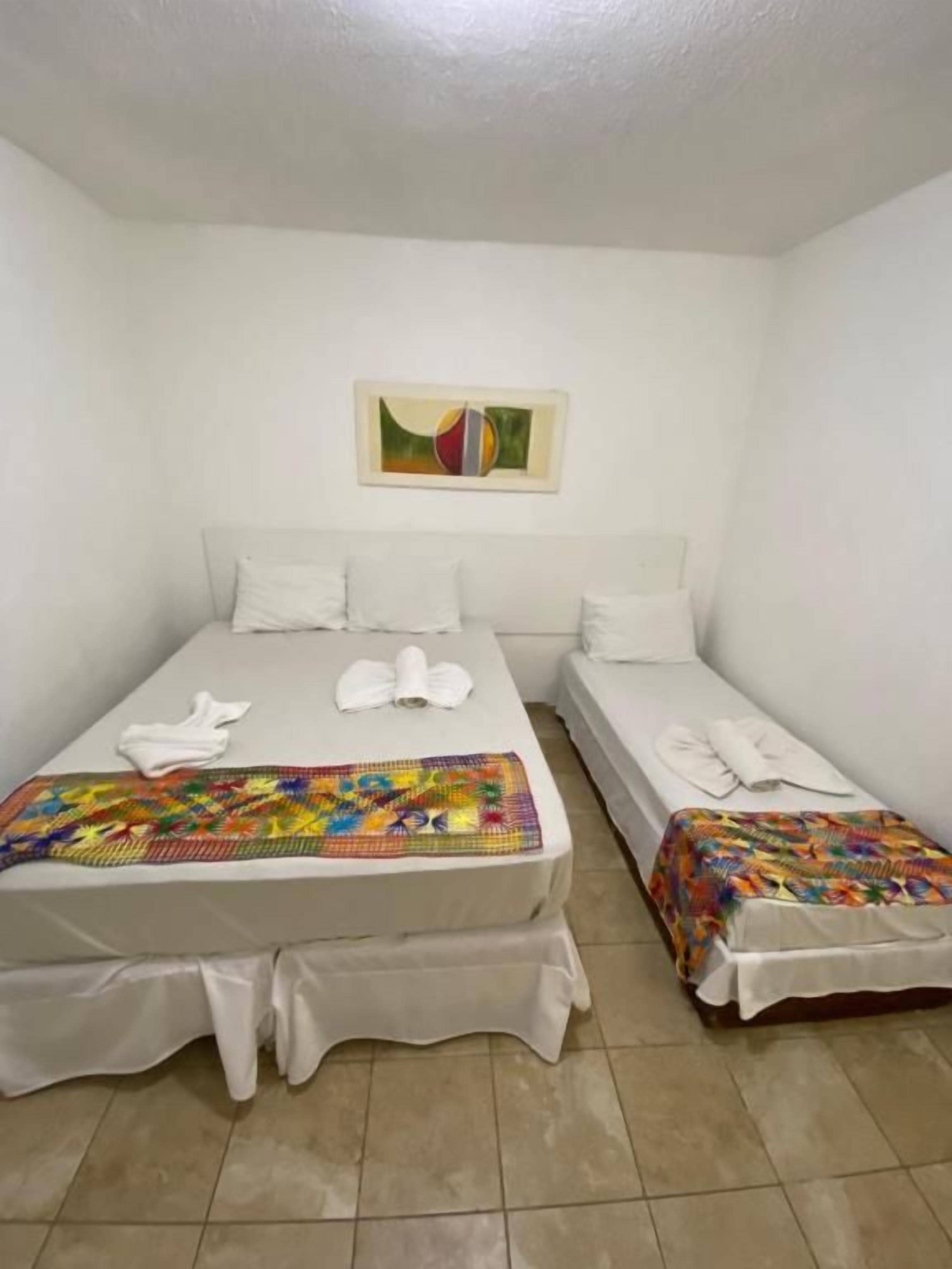 Une chambre avec deux lits, chacun recouvert d’une couverture colorée et de draps blancs.