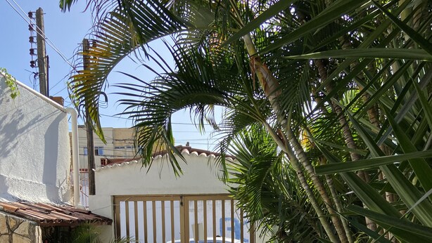 A gated entrance with a car parked inside, surrounded by potted plants and a tiled pathway. - Pousada Nossa Casa (Maceió)