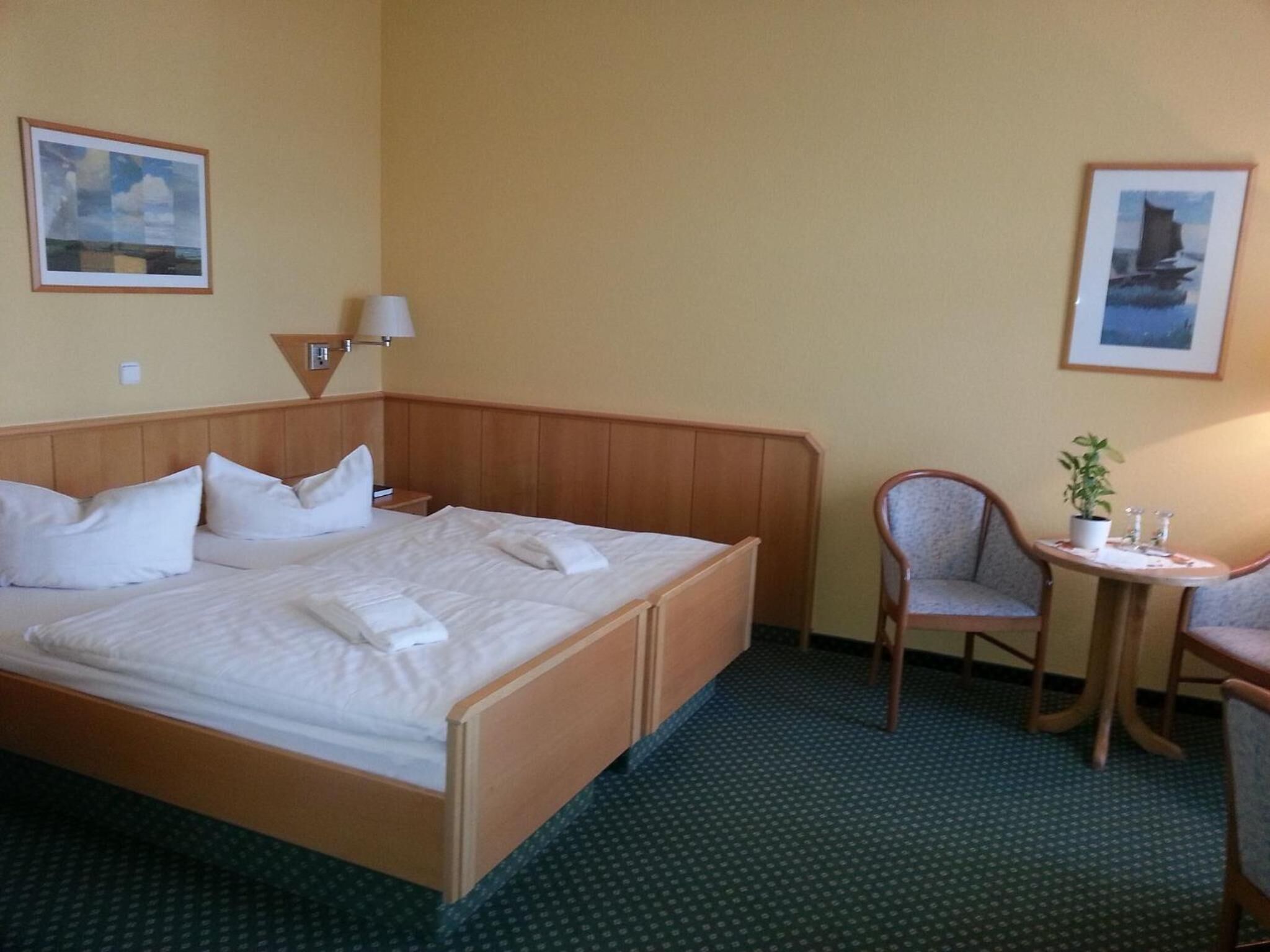 Een hotelkamer met een houten bed, een kleine tafel met een stoel, en twee ingelijste foto's aan de wand.