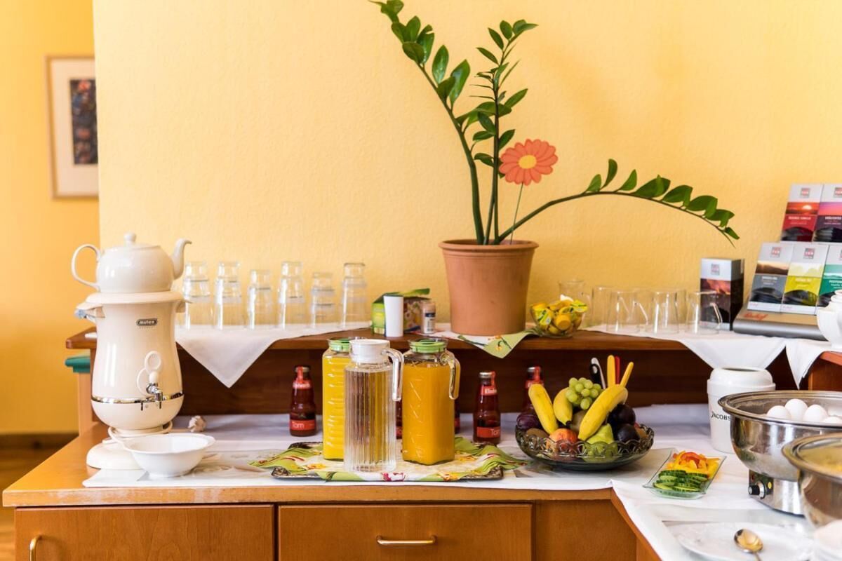 A breakfast setup with a coffee maker, juice pitchers, a fruit bowl, and a potted plant.