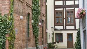 Un estrecho callejón adoquinado con un edificio de ladrillo a la izquierda y un edificio con entramado de madera a la derecha. Hay una pequeña mesa y una silla frente al edificio con entramado de madera.