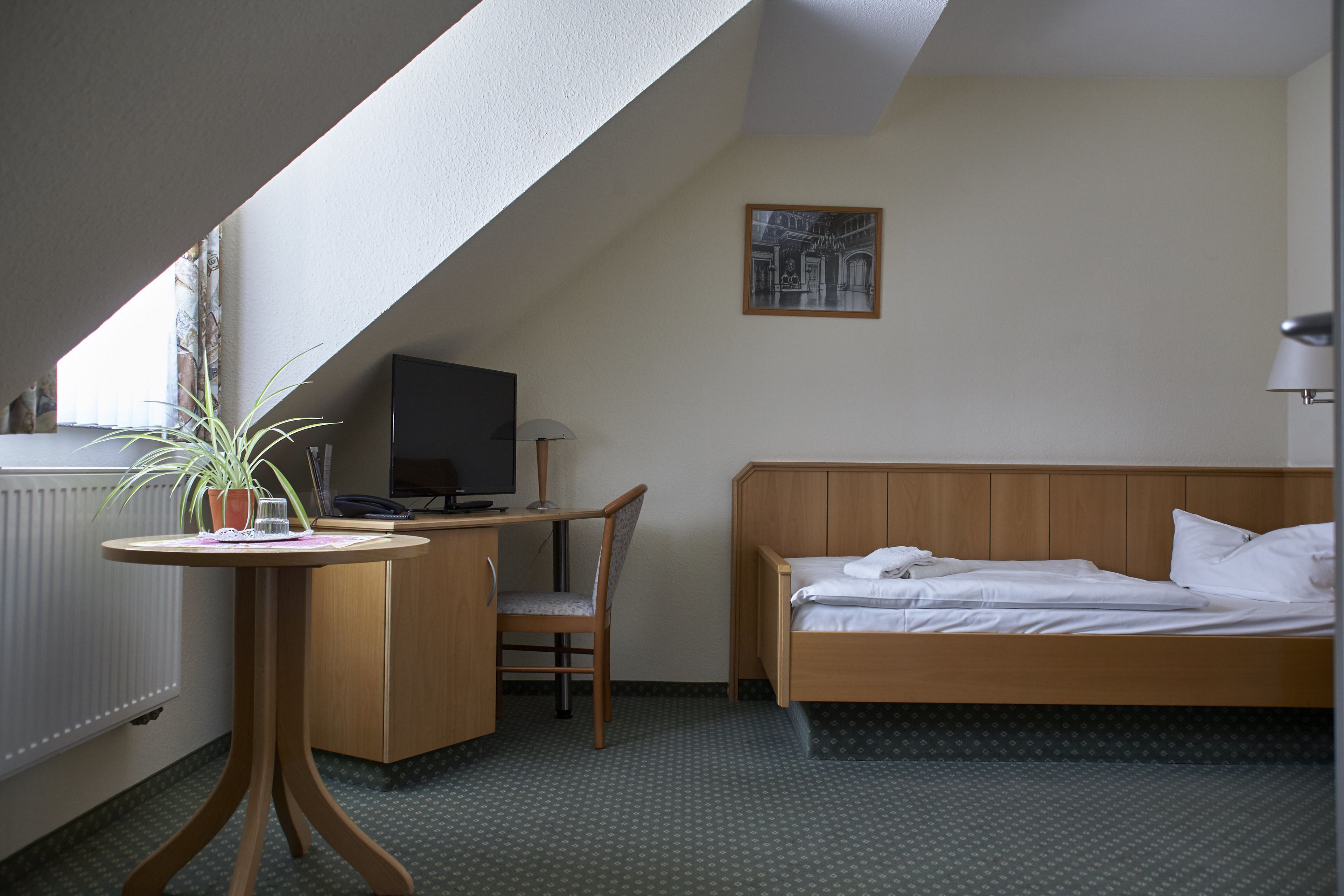 Une chambre d’hôtel équipée d’un lit, d’un bureau, d’une chaise, d’une télévision et d’une plante en pot.