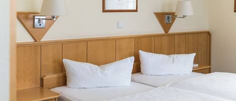 A hotel room with two beds, wooden headboard, bedside tables with lamps, and a framed picture on the wall.