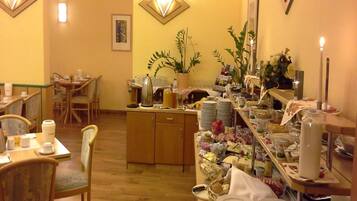 A dining area with wooden tables and chairs, a buffet setup with various food items, and wall-mounted light fixtures.