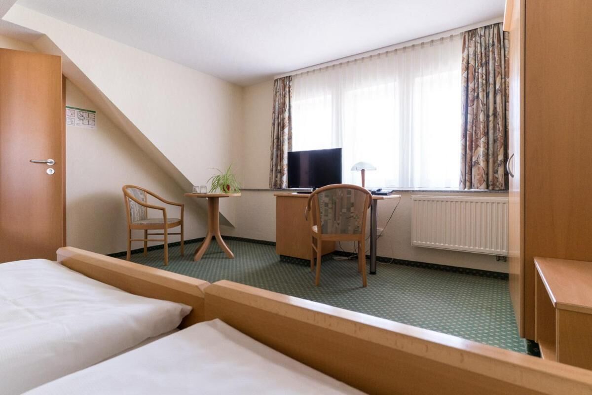 A hotel room with a bed, a desk, a chair, a television, and a window with curtains.