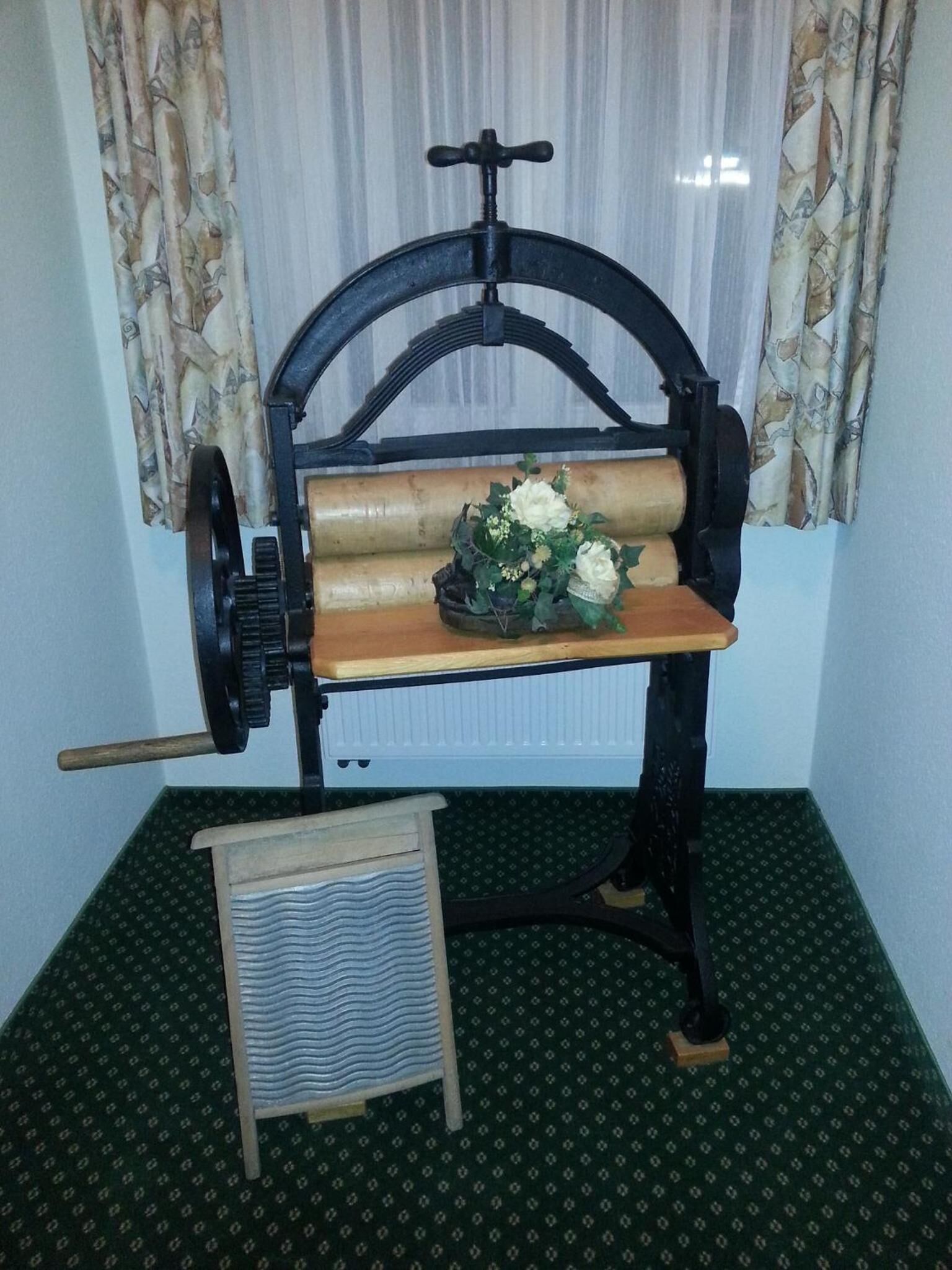 Une machine à coudre ancienne à manivelle, avec une table en bois, une bobine de fil et un petit tabouret en bois placé devant.