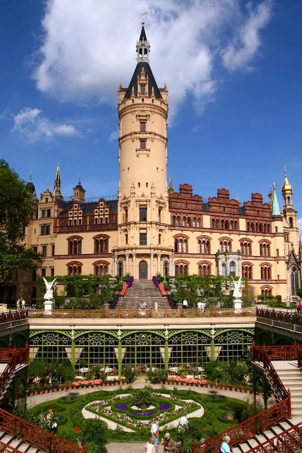 A historic building with a prominent tower, ornate architecture, and a well-maintained garden with a central fountain. - Hotel Am Schloß (Schwerin)