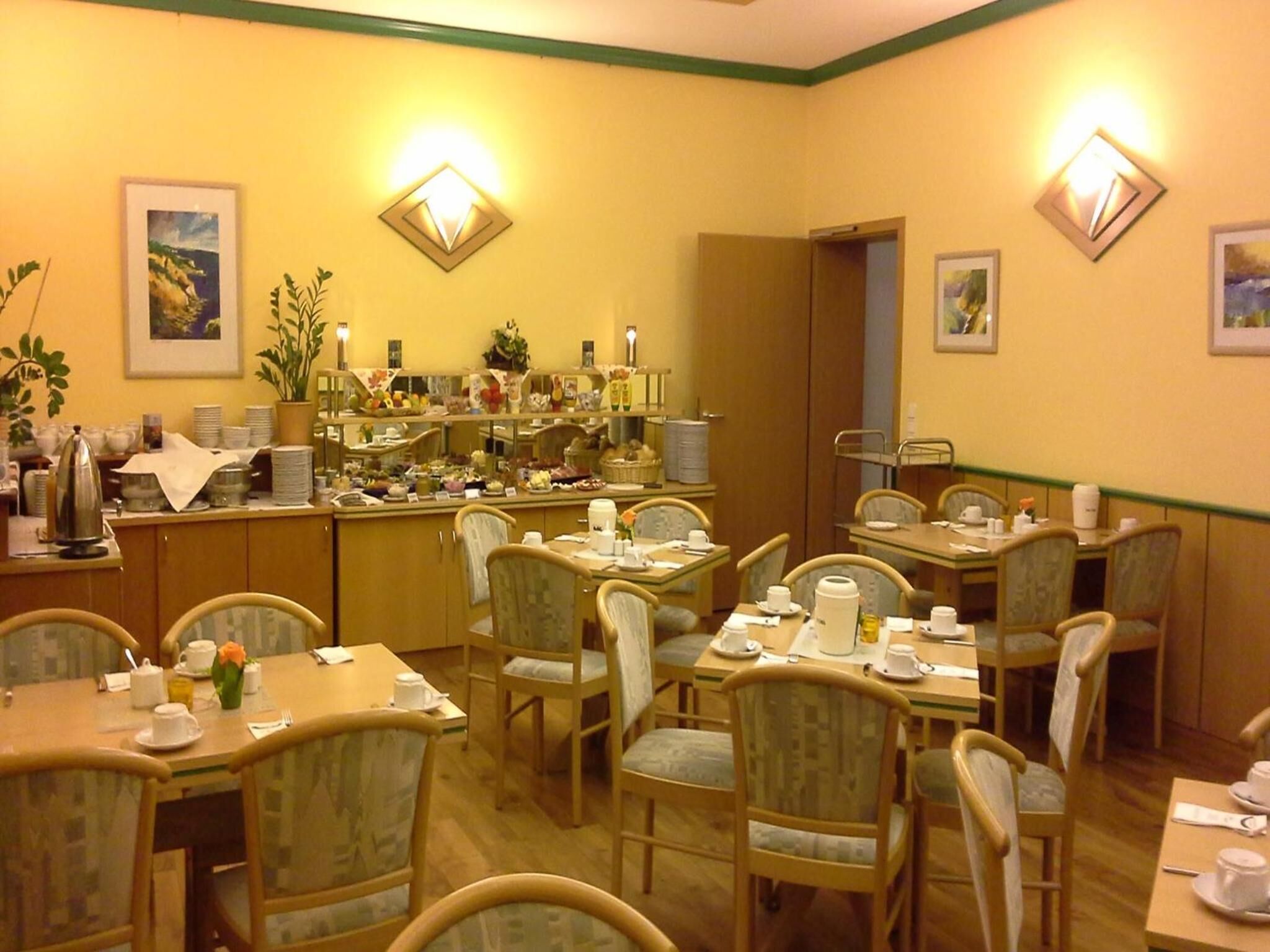 A dining area with wooden tables and chairs, a buffet counter with various food items, and wall-mounted light fixtures.