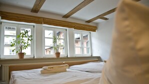 Habitación de hotel con una cama, dos plantas en macetas en el alféizar de la ventana y vistas a edificios.