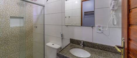 A bathroom with a glass shower enclosure, a white toilet, a granite countertop sink, a mirror, and a hairdryer mounted on the wall.