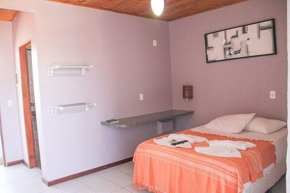 Quarto com cama, um banquinho, porta-toalhas e um quadro na parede.