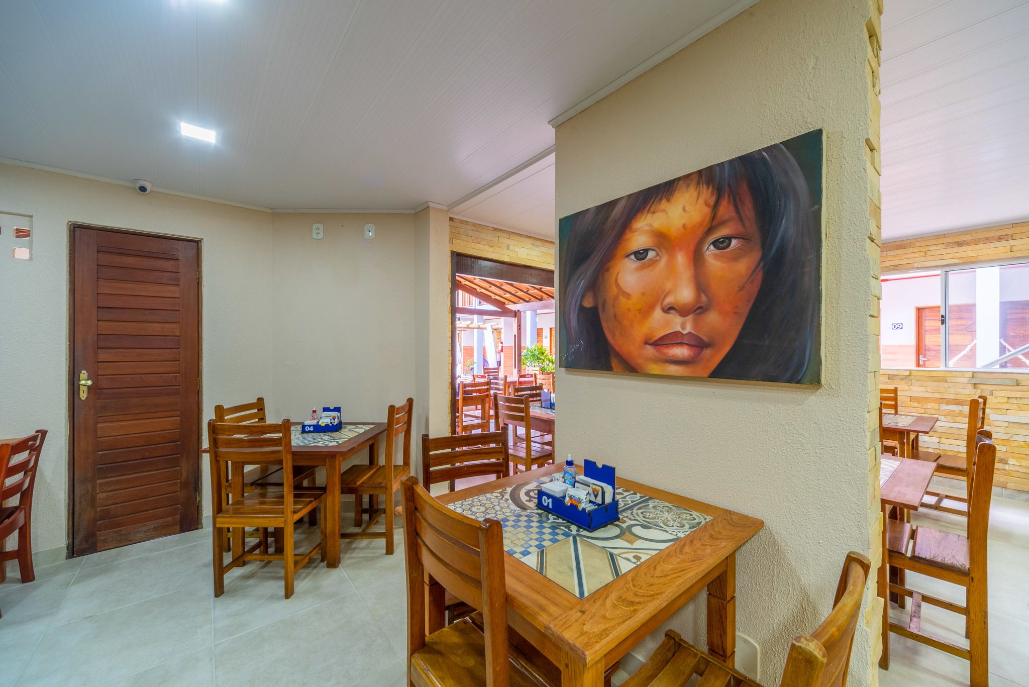 A dining area with wooden tables and chairs, a tiled floor, and a painting on the wall.