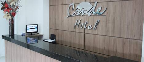 A hotel reception desk with a wooden panel backdrop and a sign that reads "Condor Hotel".