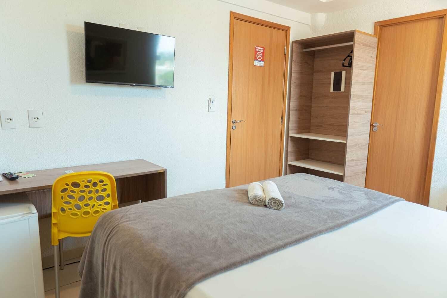 A hotel room with a bed, a desk, a chair, a TV, and a wardrobe.