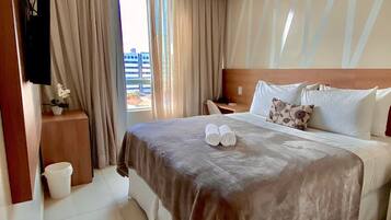 Habitación de hotel con una cama grande, una mesita de noche, un televisor montado en la pared y vistas al exterior.