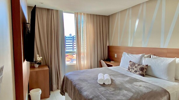 Ein Hotelzimmer mit einem großen Bett, einem Holz-Kopfende, einem Nachttisch, einem Fernseher und Blick auf Gebäude.