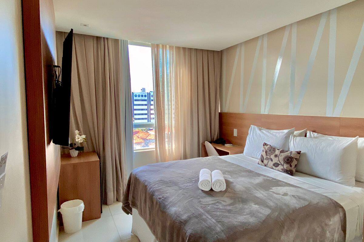 Une chambre d’hôtel avec un grand lit, une tête de lit en bois, une table de chevet, une télévision et une vue sur les bâtiments par la fenêtre.