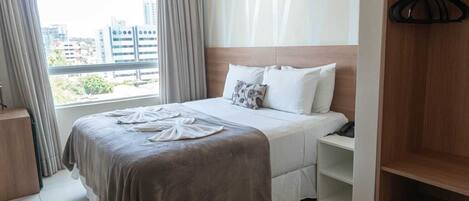 A hotel room with a bed, a bedside table, a wardrobe, and a window with curtains.