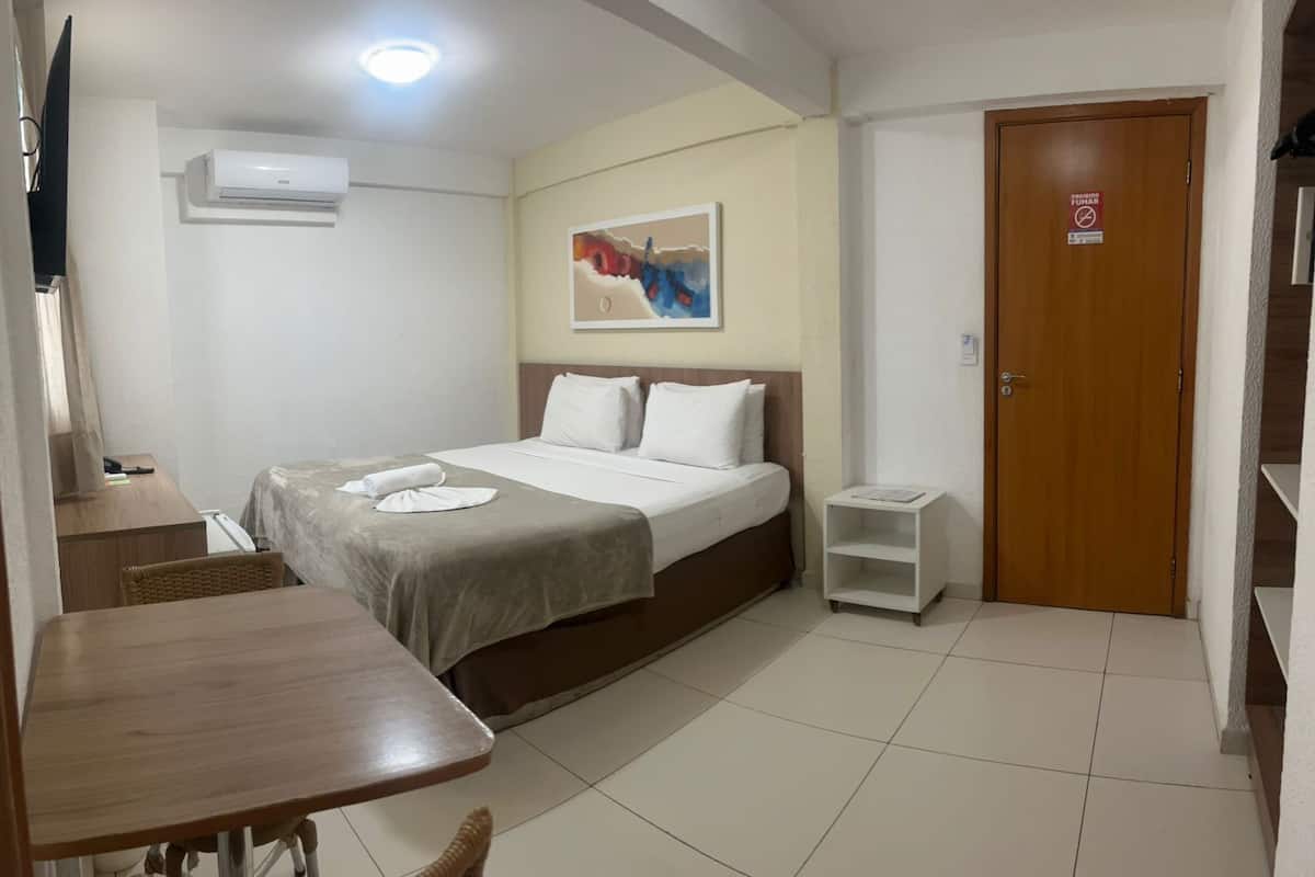 Une chambre d’hôtel avec un lit, un bureau, une chaise, une télévision, un tableau au mur et une porte avec une pancarte.