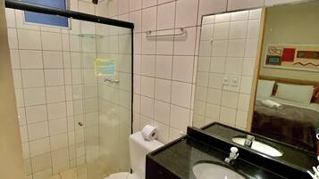 Baño con ducha de vidrio, inodoro, lavamanos con encimera negra y espejo.
