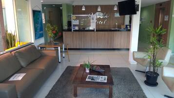 A hotel reception area with a wooden reception desk, a sofa, a coffee table, and potted plants.