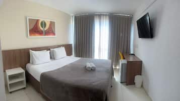 Quarto de hotel com cama, escrivaninha, televisão e um quadro na parede.