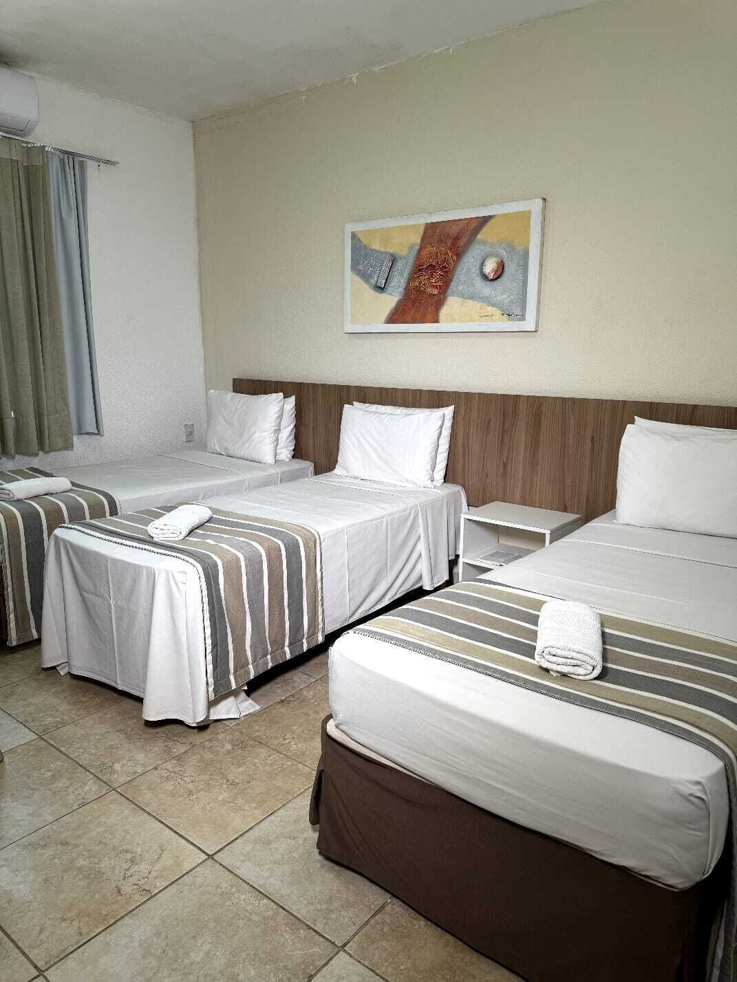 A hotel room with two beds, a wooden headboard, a painting on the wall, and a window with curtains.