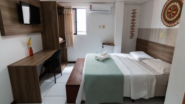 A hotel room with a bed, a desk, a chair, a bench, a TV, an air conditioner, and a window. - Hotel Pousada Gogo da Ema (Maceió)