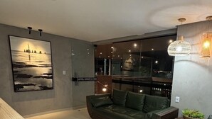 A modern living room with a green sofa, a wicker ottoman, and a large painting of a lighthouse. - Hotel Pousada Gogo da Ema (Maceió)