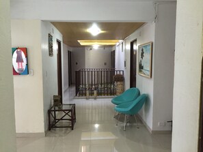 A hallway with a glass table, teal chairs, and a railing.