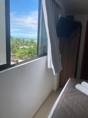 Un dormitorio con un ventanal grande, una cama y vistas a una playa y palmeras.