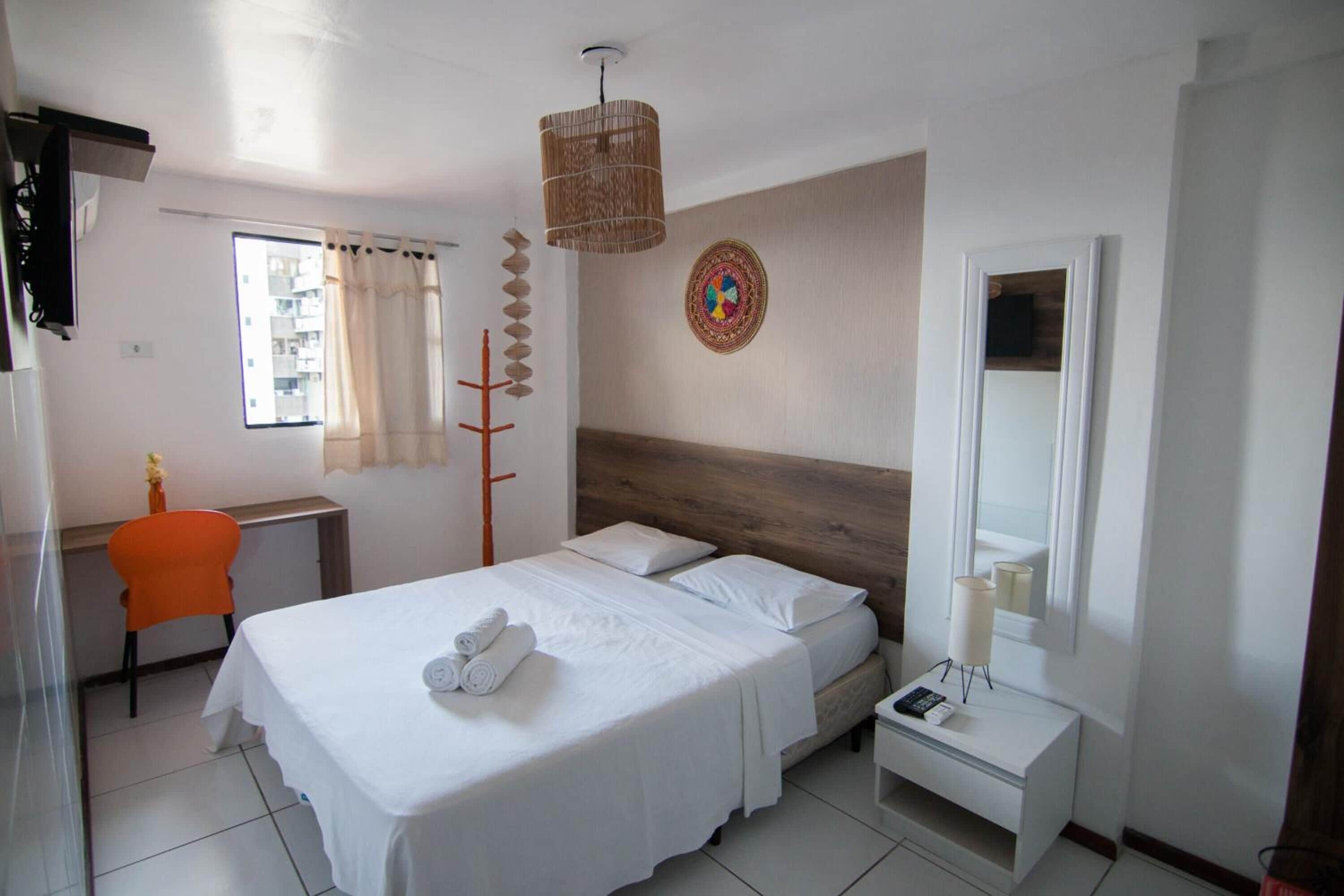 A hotel room with a bed, bedside table, chair, and a large window with curtains.