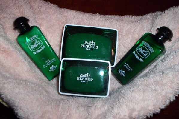Three green Hermès Paris perfume bottles on a soft, textured surface.