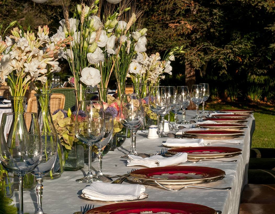 A table set for a formal outdoor event with glassware, plates, and floral centerpieces.