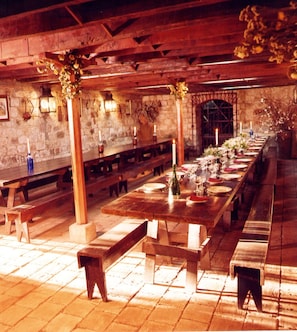 A long wooden table set for dining with benches on either side, stone walls, and a stone archway in the background.