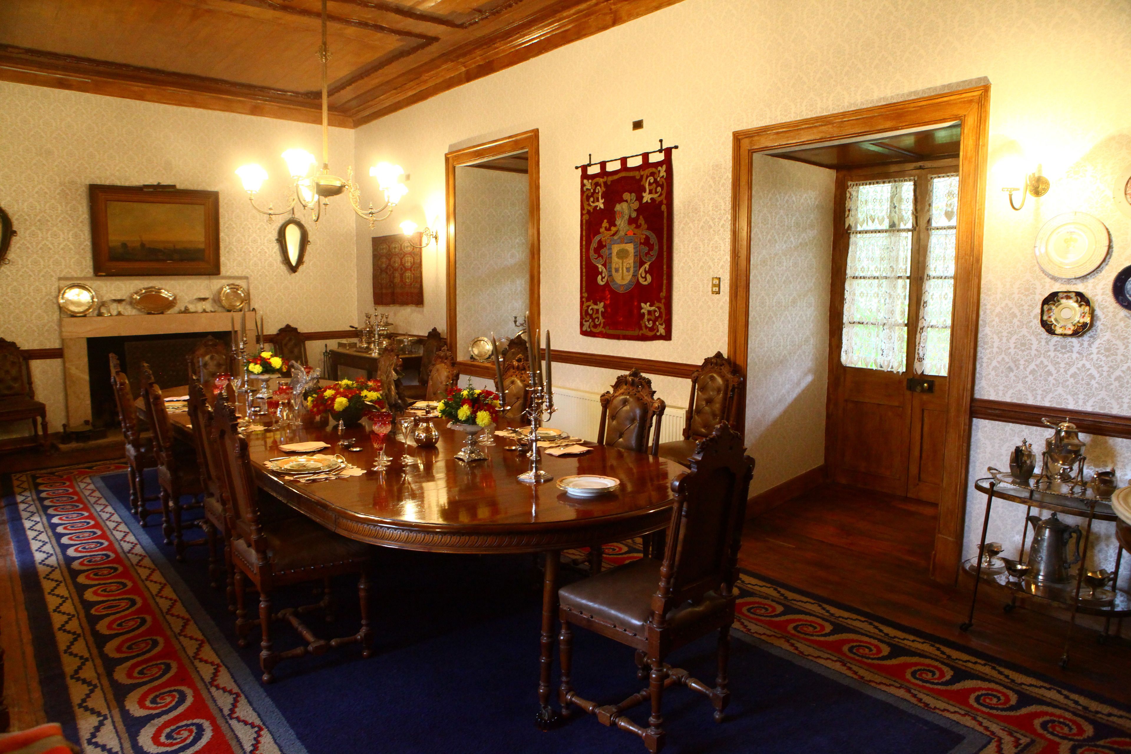 A formal dining room with a large wooden table, ornate chairs, and a red banner.