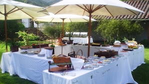 Een buffetopstelling buiten, met meerdere tafels bedekt met witte tafelkleden, omringd door grote parasols.