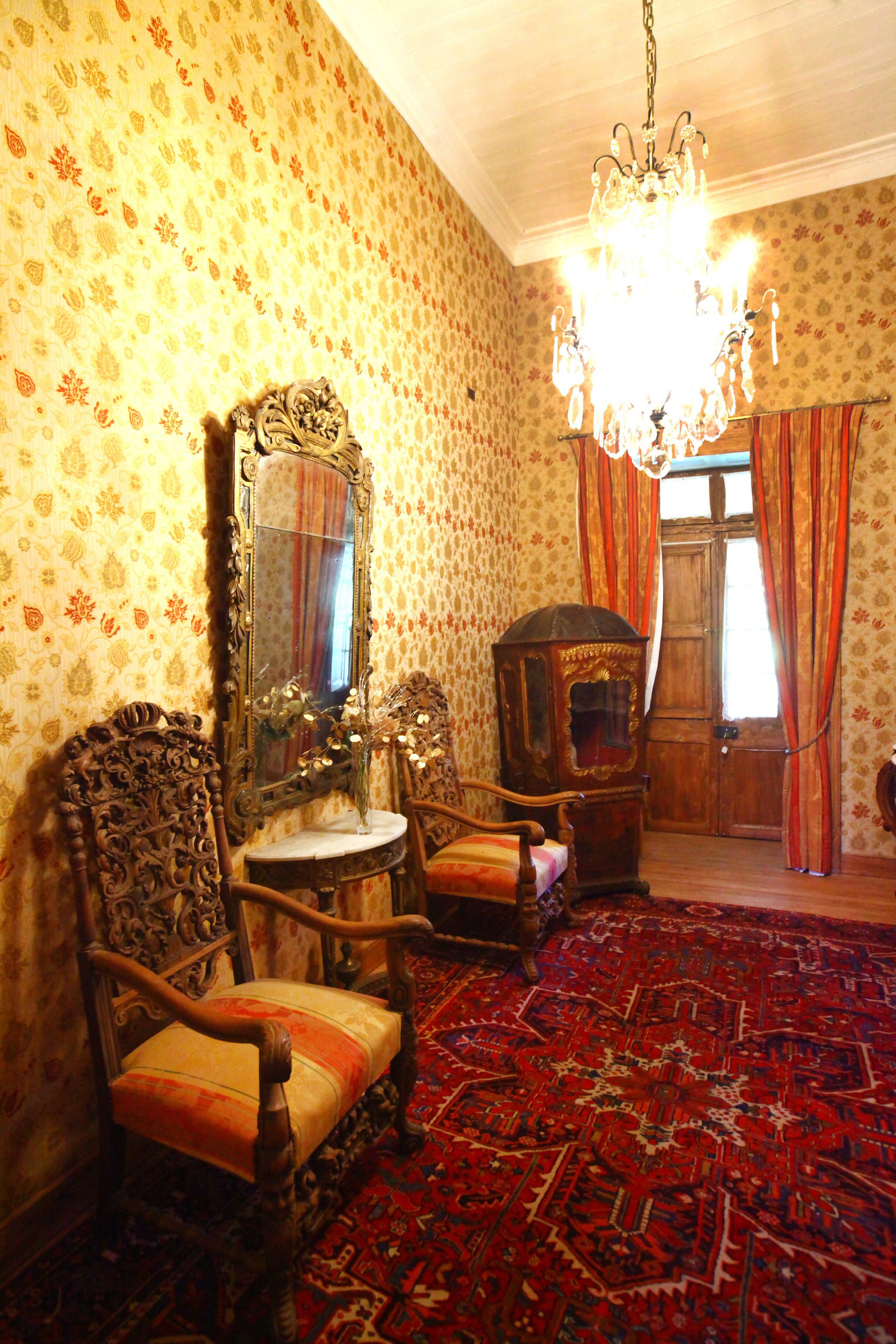 A room with ornate furniture, a chandelier, and patterned wallpaper.