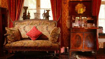 A vintage-style room with a floral-patterned sofa, a wooden cabinet with glassware, and a large mirror.
