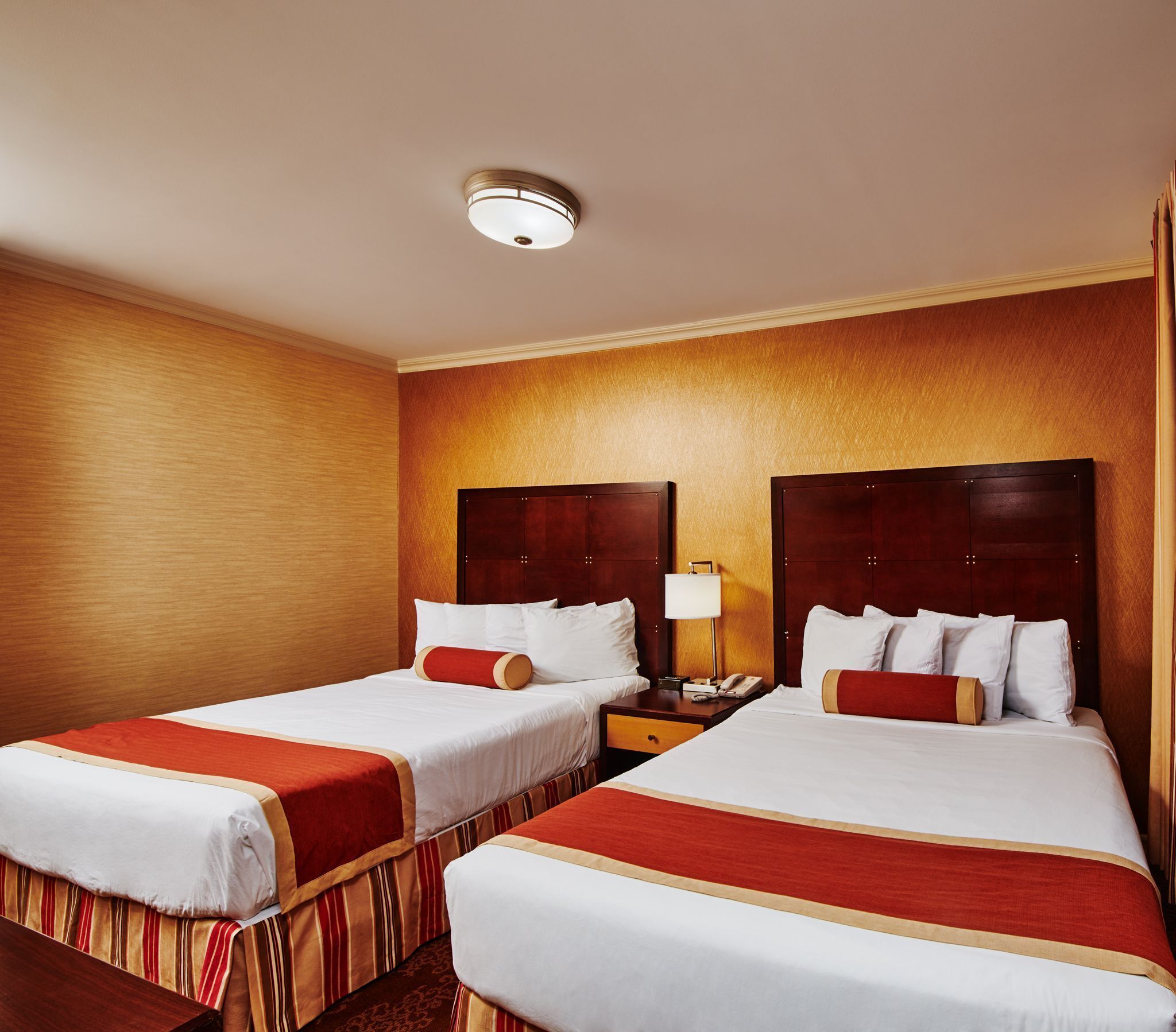A hotel room with two beds, each with a wooden headboard, a nightstand with a lamp, and a ceiling light.