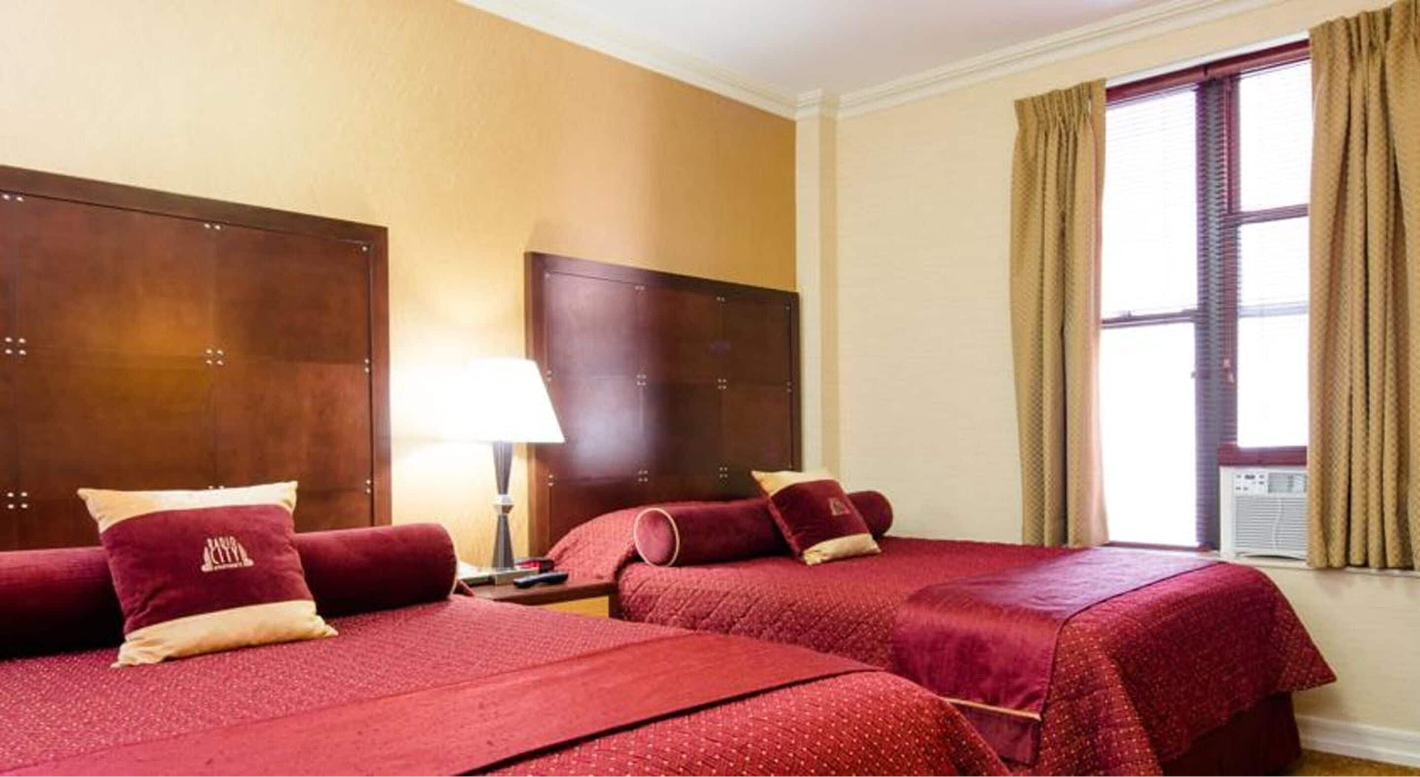 Ein Hotelzimmer mit zwei Betten, einem Nachttisch, einer Lampe und einem Fenster mit Vorhängen.