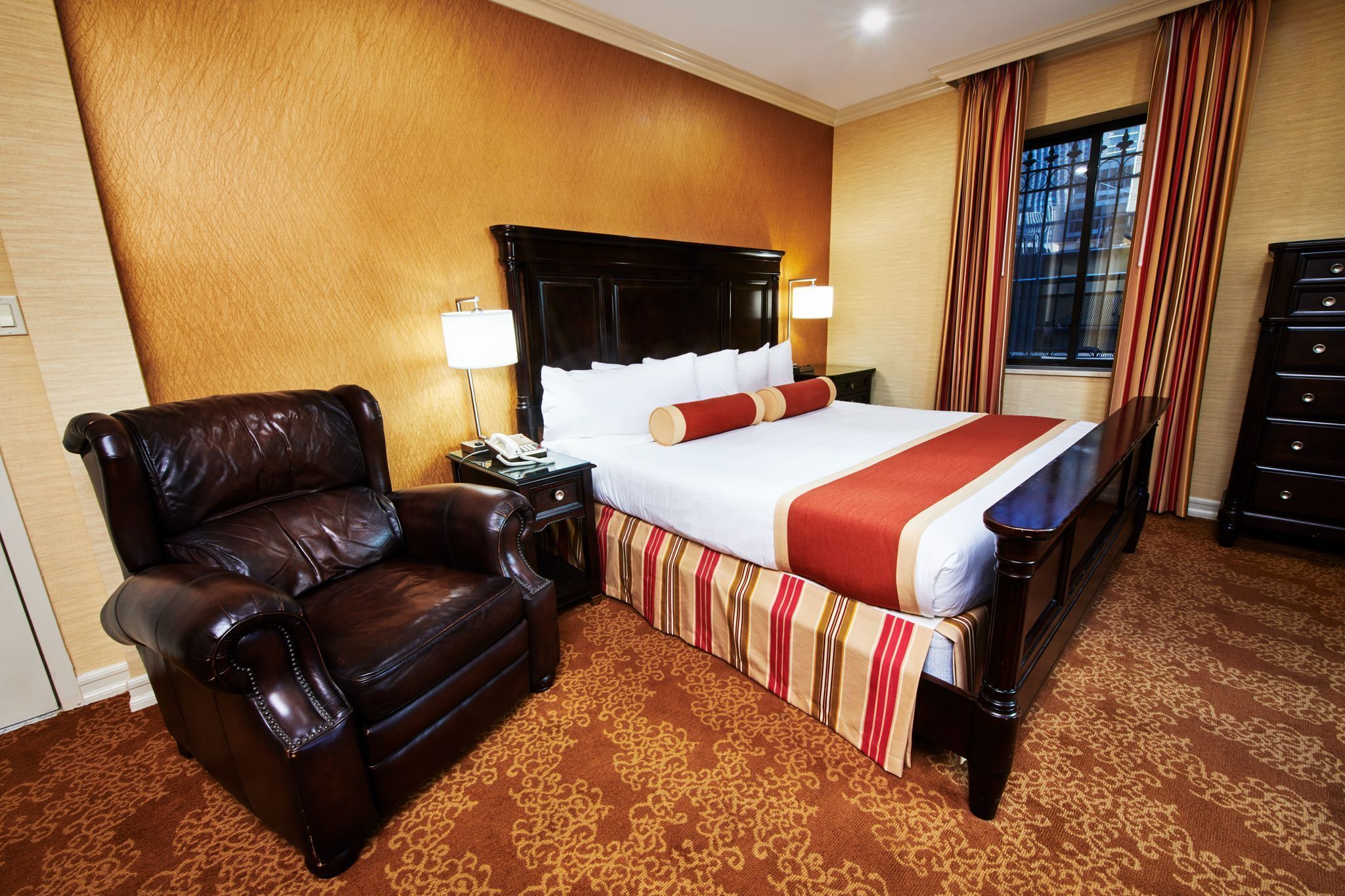 A hotel room with a large bed, a leather armchair, a nightstand, and a dresser.