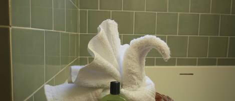 A bathroom with green tiles, a white towel, and a bottle of shampoo.