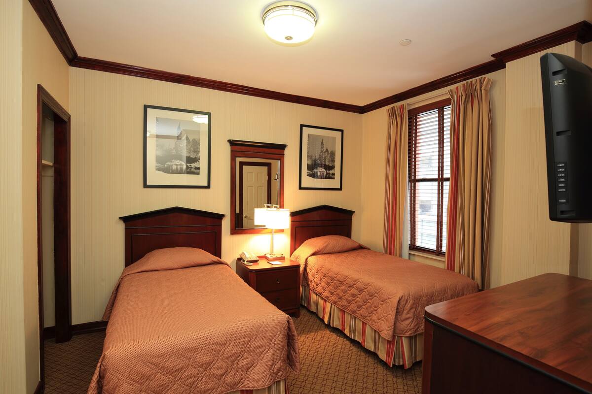 A hotel room with two beds, a nightstand with a lamp, a television, and framed pictures on the wall.