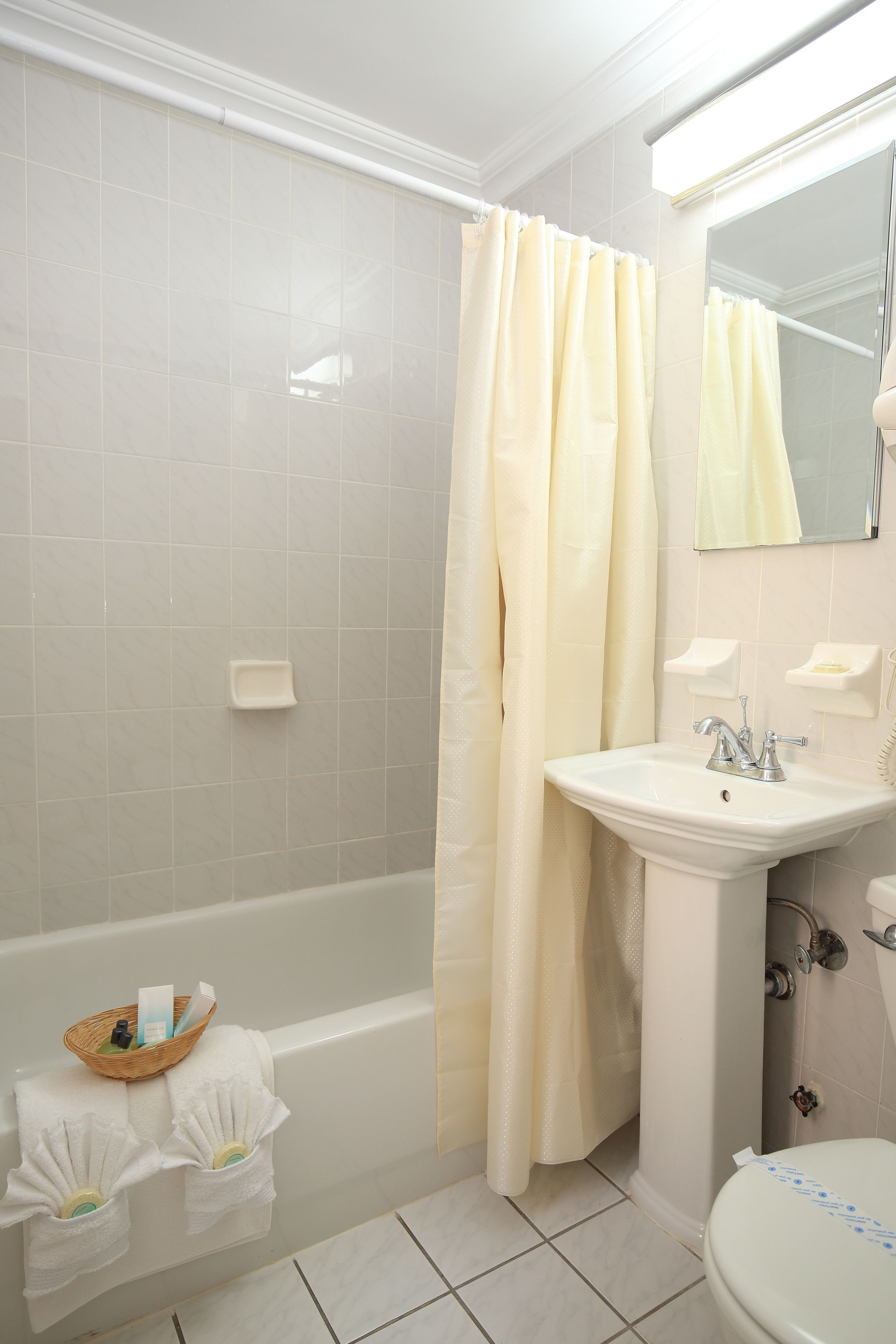 Een badkamer met een bad, een wastafel en een toilet. Handdoeken hangen aan de muur en er staat een mandje met toiletartikelen op het bad.
